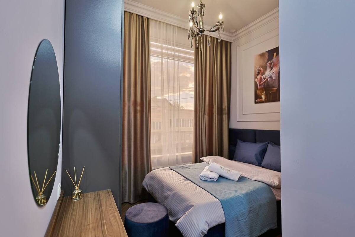 A hotel room with a bed, a mirror, a chandelier, and a painting on the wall.