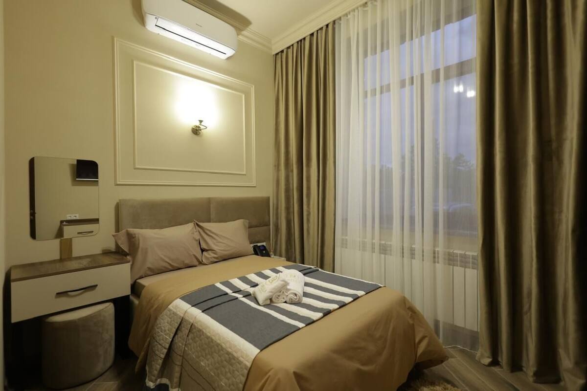 A hotel room with a bed, bedside table, and a mirror.