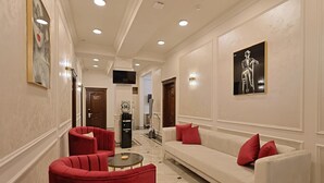 Un vestíbulo de hotel con un sofá blanco, sillas rojas, una mesa redonda y obras de arte en las paredes.