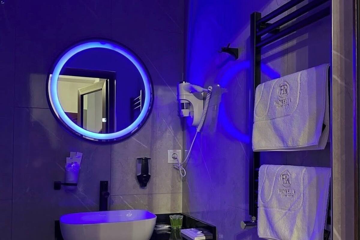 A modern bathroom with a round mirror, a sink, a hairdryer, and towels hanging on a rack.