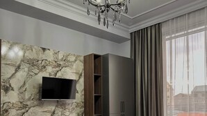 Une chambre d’hôtel moderne avec un mur en marbre, un téléviseur à écran plat, une armoire, un lit recouvert d’une couverture à rayures et une grande fenêtre avec des rideaux.