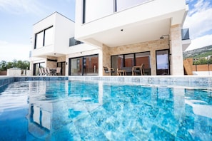 A modern two-story house with a swimming pool, outdoor seating, and a view of the landscape. - Modern Sea View Villa, Private Pool, Jacuzzi & Sauna – Near Beach (Split/Trogir) (Kaštel Stari)
