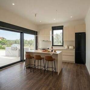 Cozinha moderna com ilha central, banquetas, geladeira preta e vista para o exterior.