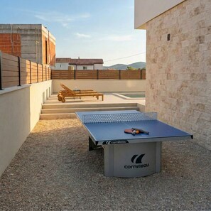 A ping pong table with a logo, a wooden bench, and a staircase leading to a building.