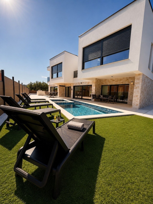 A modern two-story house with a swimming pool, outdoor seating, and a well-maintained lawn.