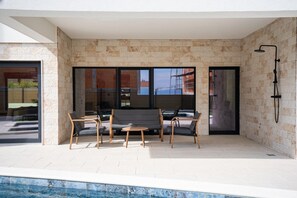 Un área de estar al aire libre con piscina, paredes de piedra y una ducha moderna.