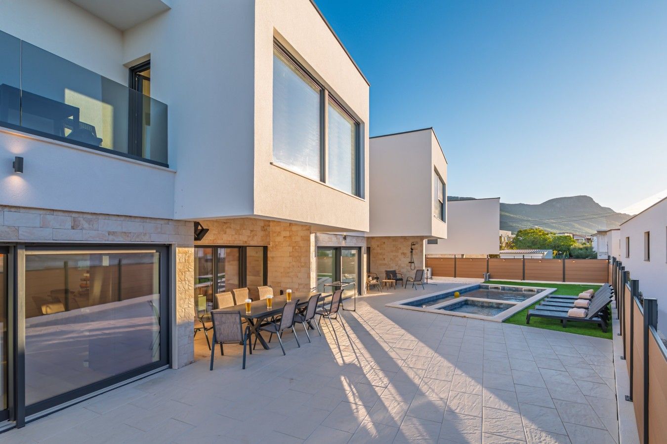 Ein modernes, zweistöckiges Haus mit Terrasse, Sitzgelegenheiten im Freien und einem Swimmingpool.