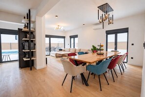 A spacious dining area with a wooden table and colorful chairs, a built-in bookshelf, and large windows offering a view.