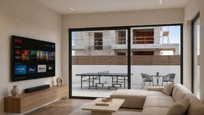 A modern living room with a flat-screen TV, a sofa, a coffee table, and a view of an outdoor area with a ping pong table and chairs. - Luxury Villa Heated Whirl/Pool · Sea View · AC · WIFI · Parking – Near Beach (Split/Trogir) (Kaštel Stari)