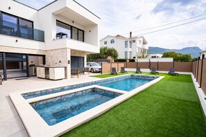 A modern two-story house with a swimming pool, outdoor seating, and a view of the mountains.