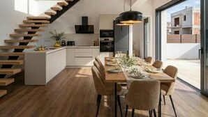 A modern kitchen with a wooden staircase, a dining area with a long table and chairs, and a large window offering a view of the outside. - Luxury Villa Heated Whirl/Pool · Sea View · AC · WIFI · Parking – Near Beach (Split/Trogir) (Kaštel Stari)