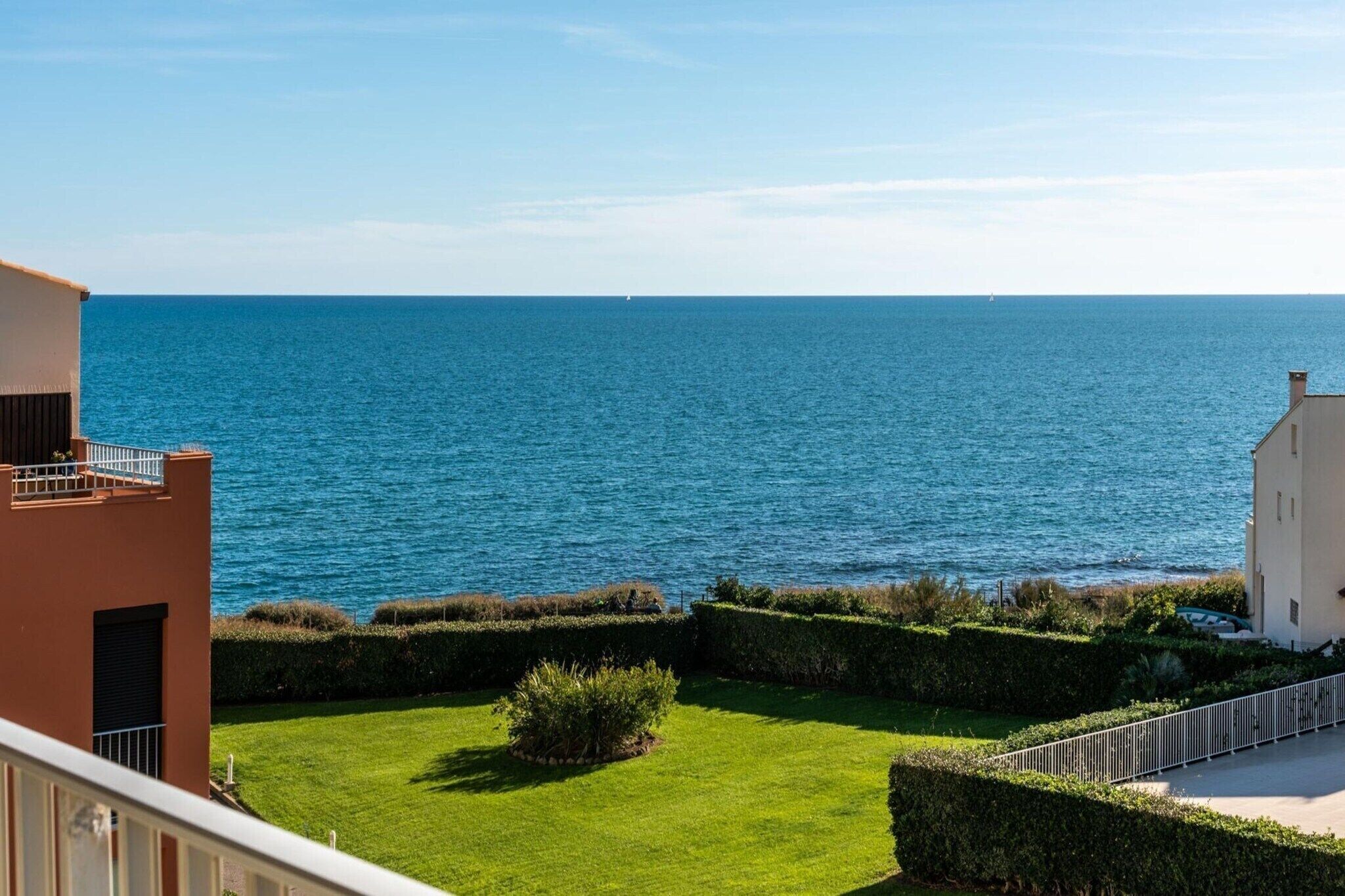 Blick auf die Küste mit blauem Himmel, einer grünen Wiese und einem Gebäude mit einem Balkon mit Meerblick.