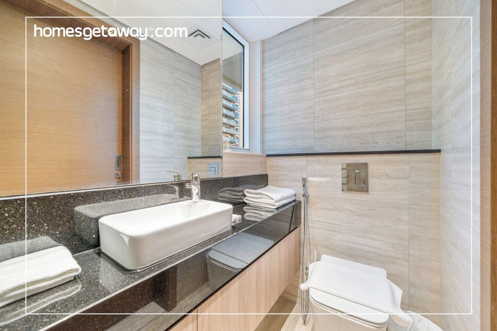 A modern bathroom with a large mirror, a white sink, and a toilet.