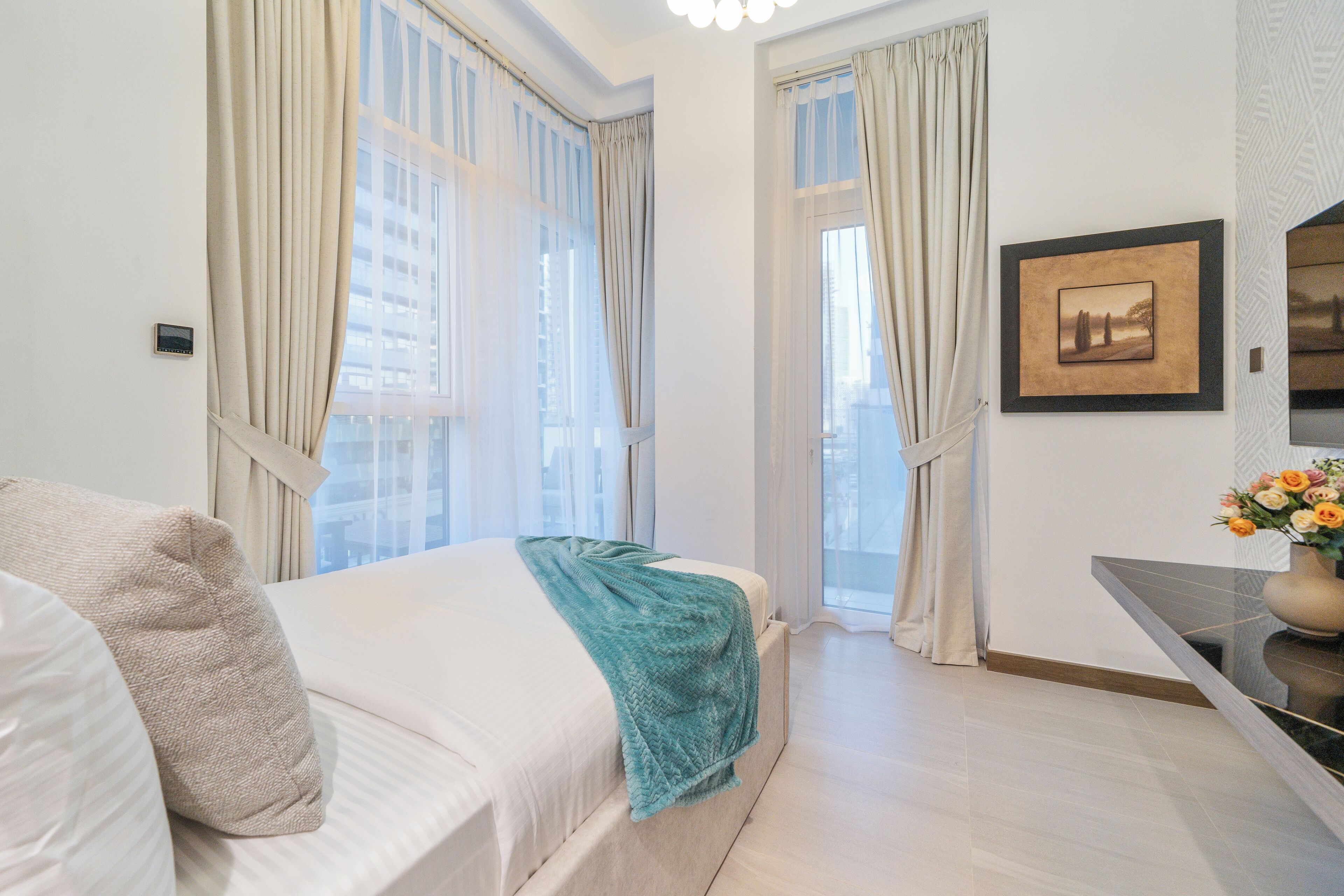Habitación de hotel moderna con una cama grande, un pequeño rincón de descanso y vistas de la ciudad a través de amplios ventanales.