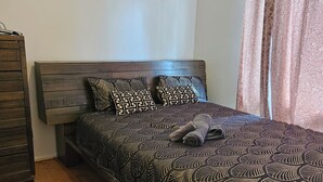 Een slaapkamer met een houten hoofdbord, een bed met een versierd sprei, twee kussens, een nachtkastje, een dressoir van hout, en een tapijt met patroon.