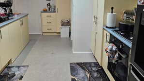Een keuken met beige kastjes, een zwart fornuis en een kleine koelkast.