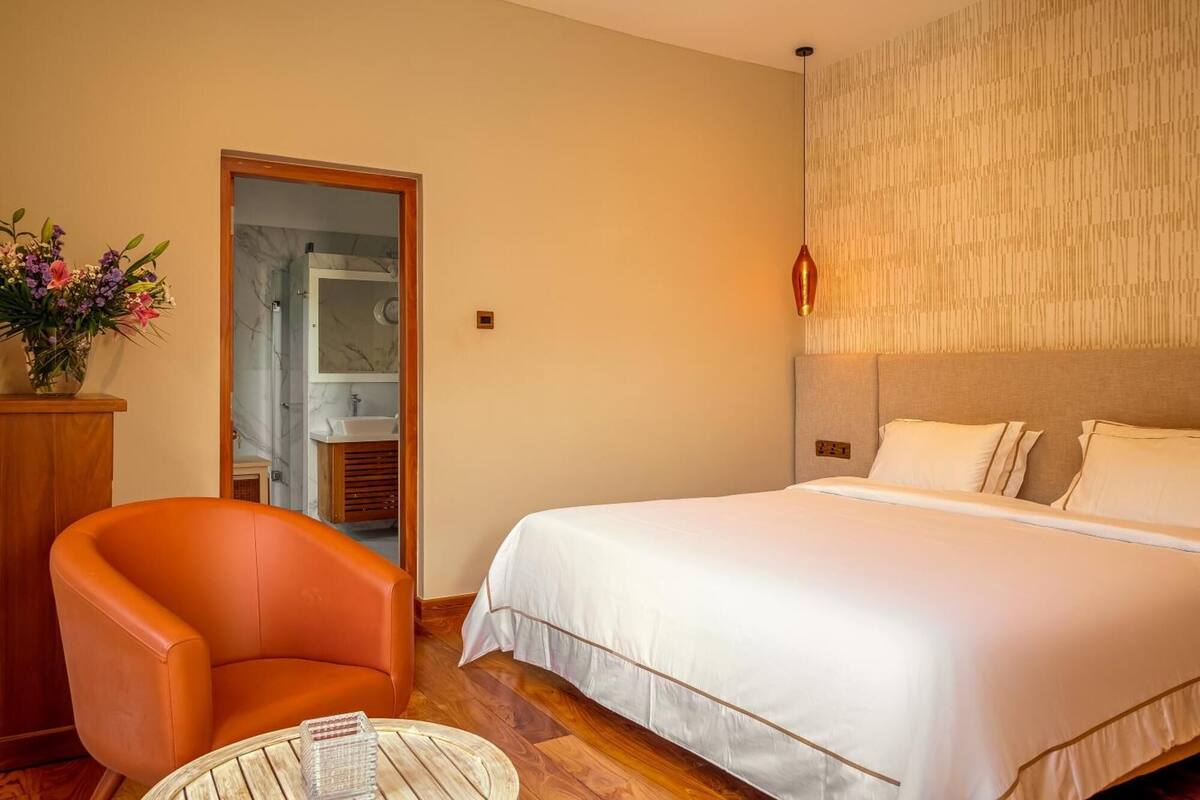 Ett hotellrum med en säng, en stol, ett litet bord, en spegel och ett badrum som syns genom en öppen dörr.