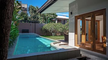 Relax by the clear pool surrounded by a well-maintained garden and a wooden deck with a bench.