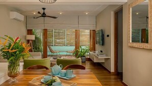 Un soggiorno moderno con pavimento in legno, una ventola a soffitto, un tavolo da pranzo con sedie, un divano e una TV appesa al muro.