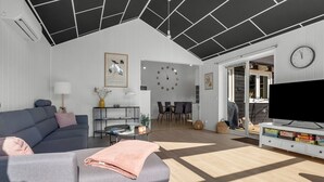 A modern living room with a grey sofa, a coffee table, a flat-screen TV, and a dining area with a clock on the wall. - "Amdi" - 1.3km from the sea by Interhome (Væggerløse)
