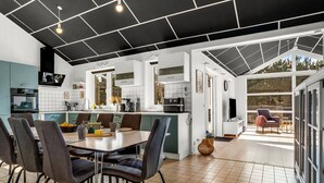 A modern kitchen with white cabinets, a dining area with dark chairs, and a large window overlooking a garden. - "Amdi" - 1.3km from the sea by Interhome (Væggerløse)