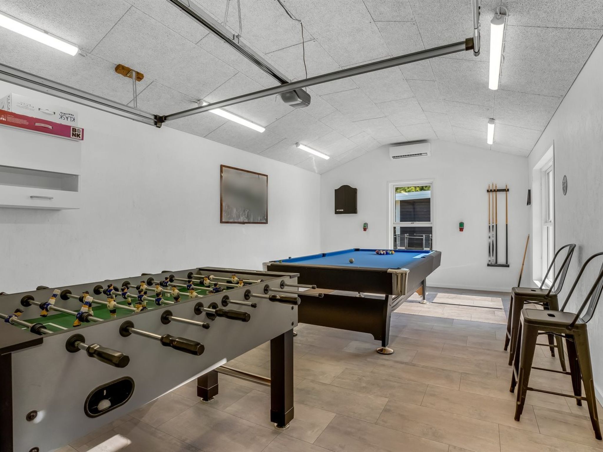 A room with a foosball table, a pool table, and a billiards rack.