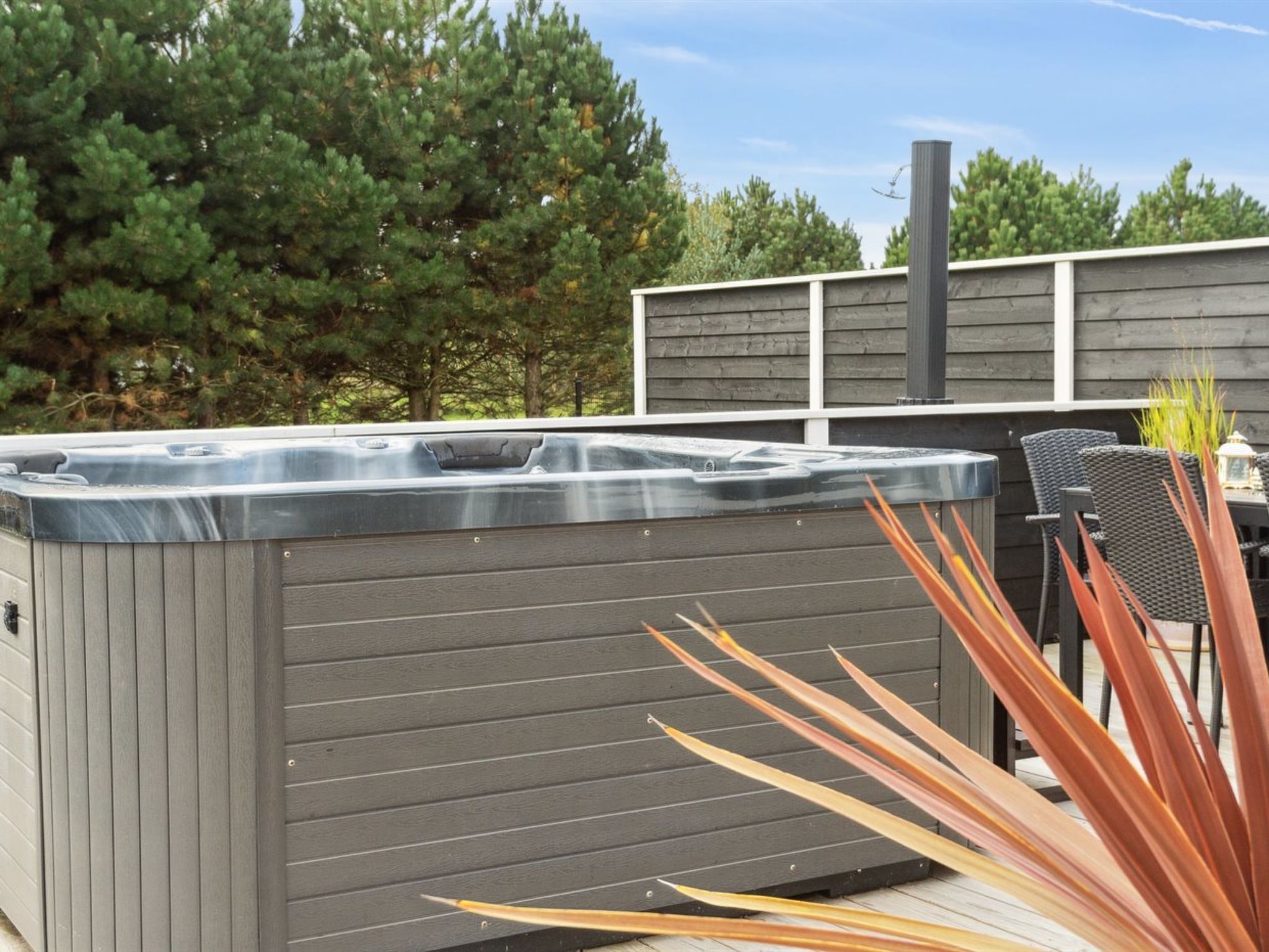 Un bain à remous avec un revêtement extérieur en bois, entouré de meubles de jardin et de plantes.