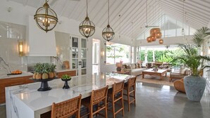 A spacious kitchen with a large island, wooden chairs, and hanging pendant lights.