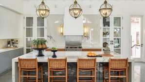 A modern kitchen with a large island, three wicker chairs, and pendant lighting.