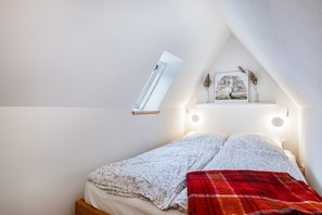 Ein Schlafzimmer mit schrägverdeckter Decke, einem Bett mit floralem Bettzeug, einer roten Decke, einer Wandleuchte und einem gerahmten Bild.