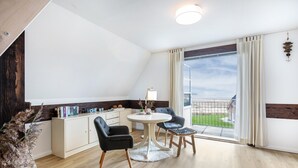 A modern room with a round table, two chairs, a white cabinet, and a view through large windows. - Apartment 'Inselliebe' with Balcony and Wi-Fi (Pellworm)