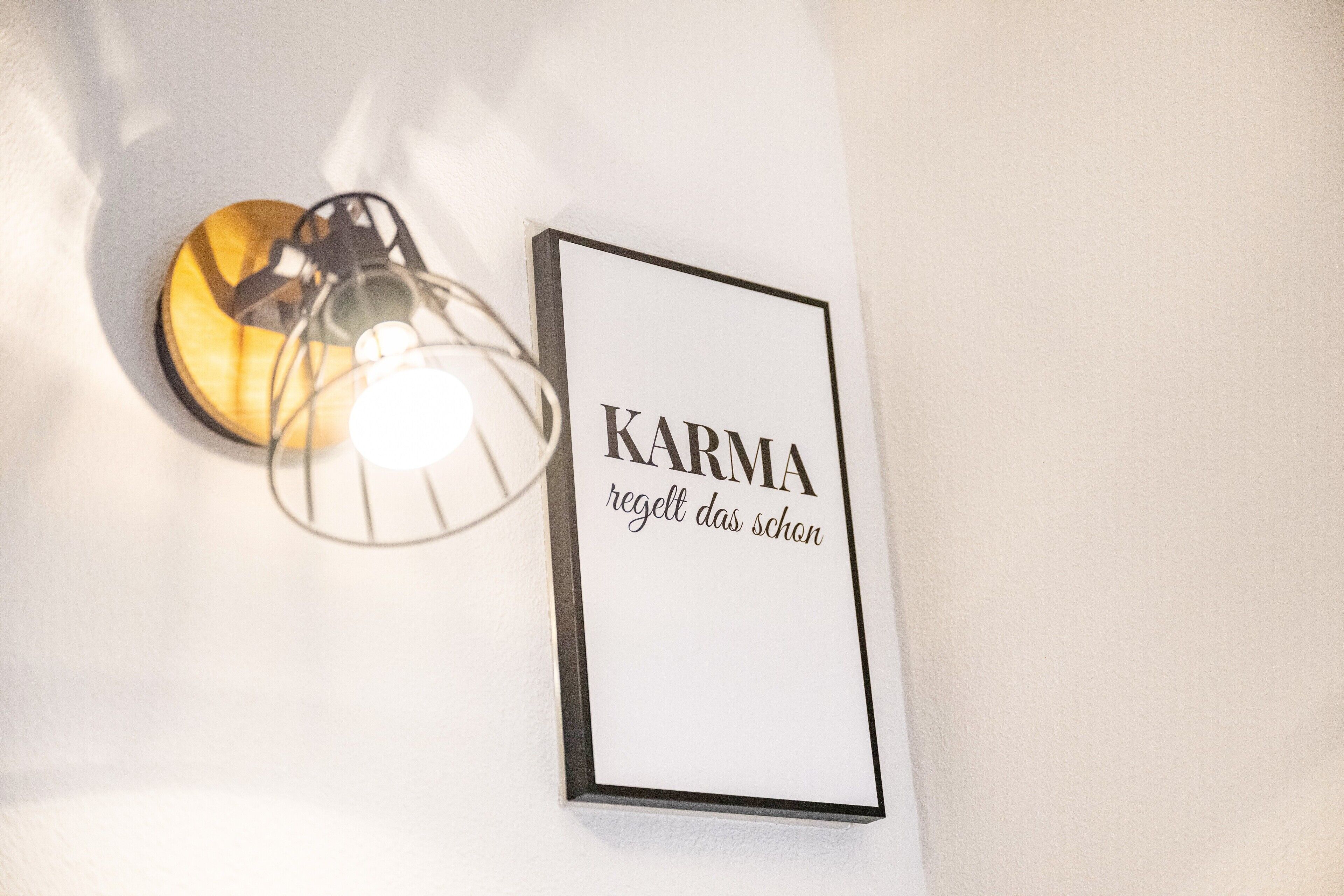 A wall-mounted light fixture with a circular shade and a framed sign with the text 'KARMA regelt das schon'.
