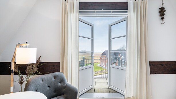 An open door leading to a balcony with a view of a building and landscape. - Apartment 'Inselliebe' with Balcony and Wi-Fi (Pellworm)