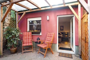 Une terrasse couverte avec deux chaises en bois, une plante en pot et une fenêtre.