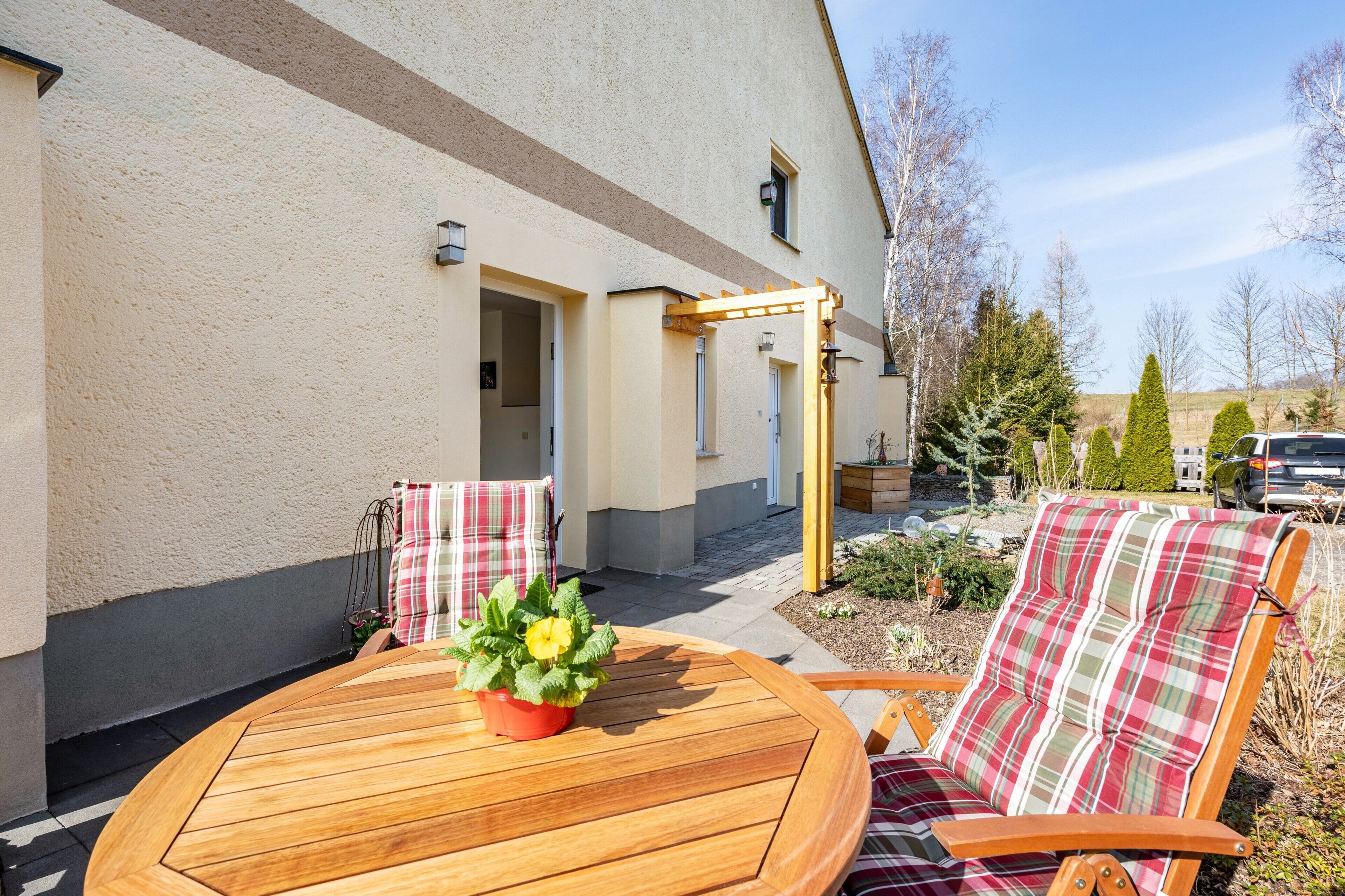 Un patio con una mesa y sillas de madera, una planta en maceta y un edificio con puerta y ventanas.