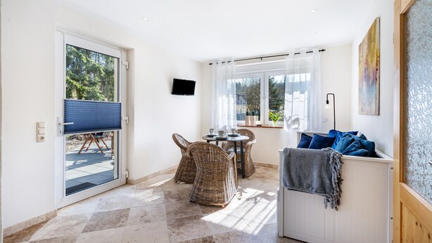 A room with a sliding glass door leading to an outdoor area, a small table with chairs, a white radiator, and a mounted television. - Apartment 'Am Miriquidi' with Mountain View, Shared Terrace and Wi-Fi (Marienberg)