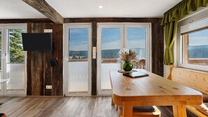 A wooden dining table with a view of the outdoors, a flat-screen TV mounted on a wooden wall, and a bench with a view of the outdoors.
