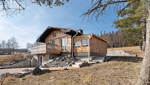 A wooden cabin with a balcony, stone steps, and a stone wall.