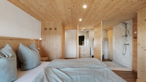 A wooden-paneled bedroom with a bed, pillows, a nightstand, a dresser, a mirror, and a shower.