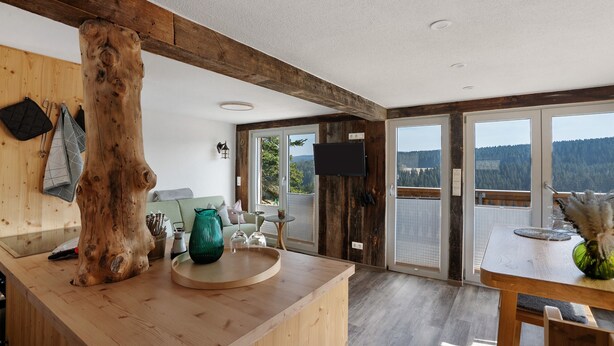 A wooden interior with a large tree trunk, a kitchen counter, and a dining area with a view.