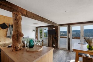 A wooden interior with a large tree trunk, a kitchen counter, and a dining area with a view. - Chalet 'Fenzl' with Mountain View, Private Terrace and Wi-Fi (Johanngeorgenstadt)