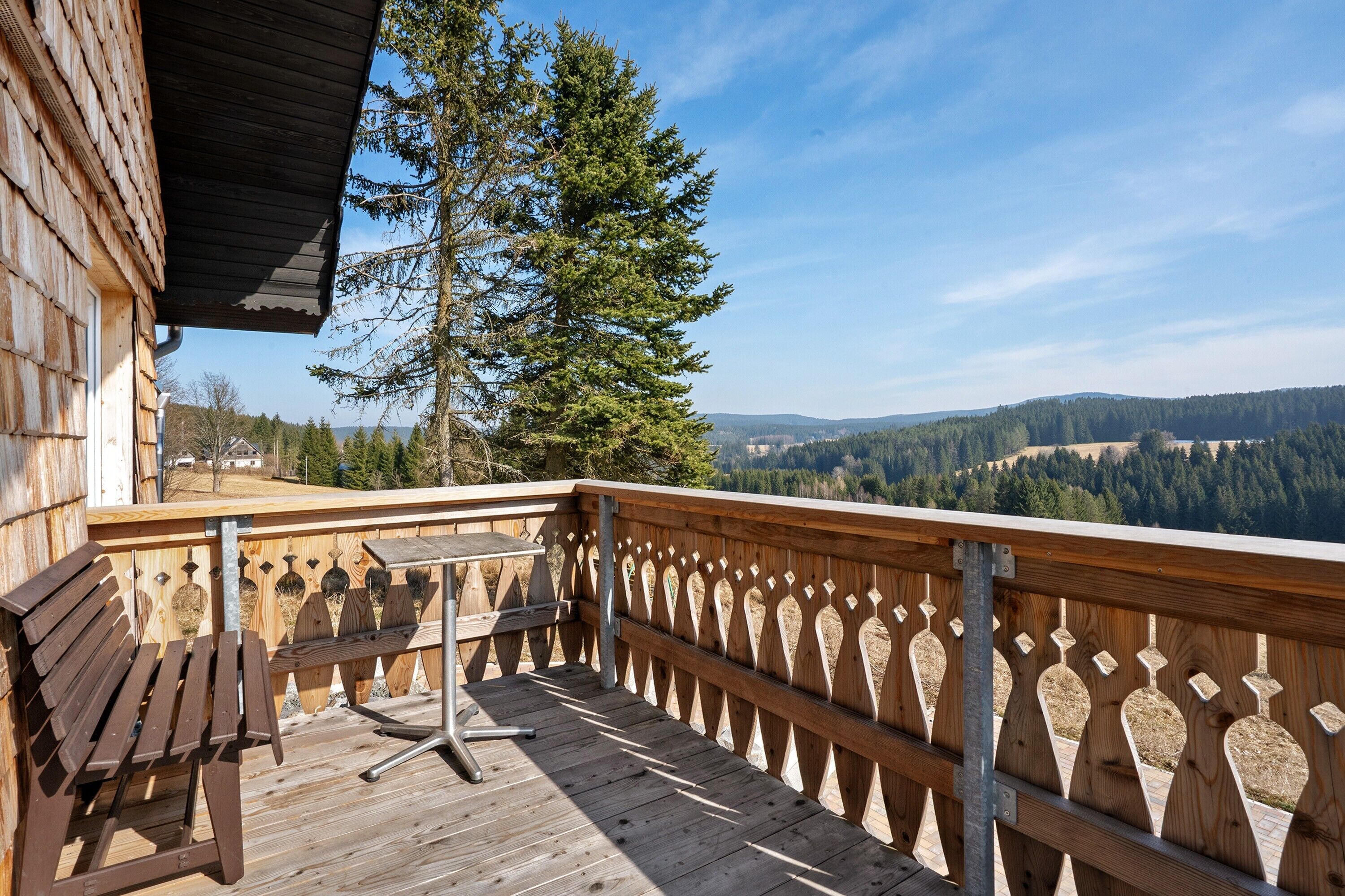 Eine Holzterrasse mit Tisch und Bank, mit Blick auf eine bewaldete Landschaft.
