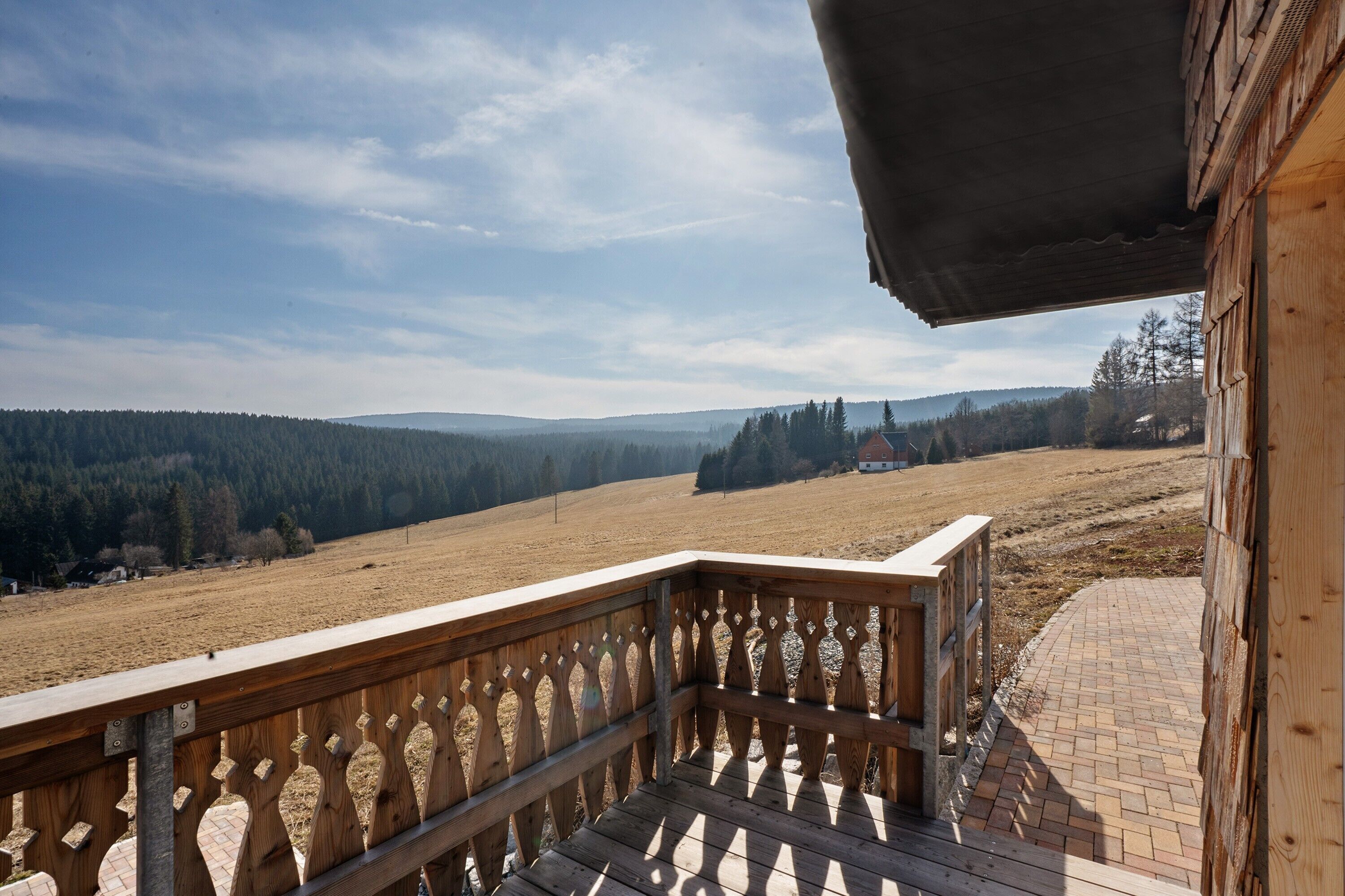Een houten balkon met uitzicht op een bebost dal en heuvels in de verte.