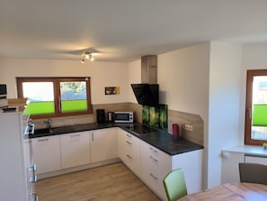 A modern kitchen with white cabinets, a black countertop, a microwave, and a coffee maker. There is a window with a view of greenery.