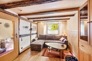Une pièce chaleureuse avec un plafond en bois, un canapé d’angle, une petite table ronde et une fenêtre donnant sur un paysage verdoyant.