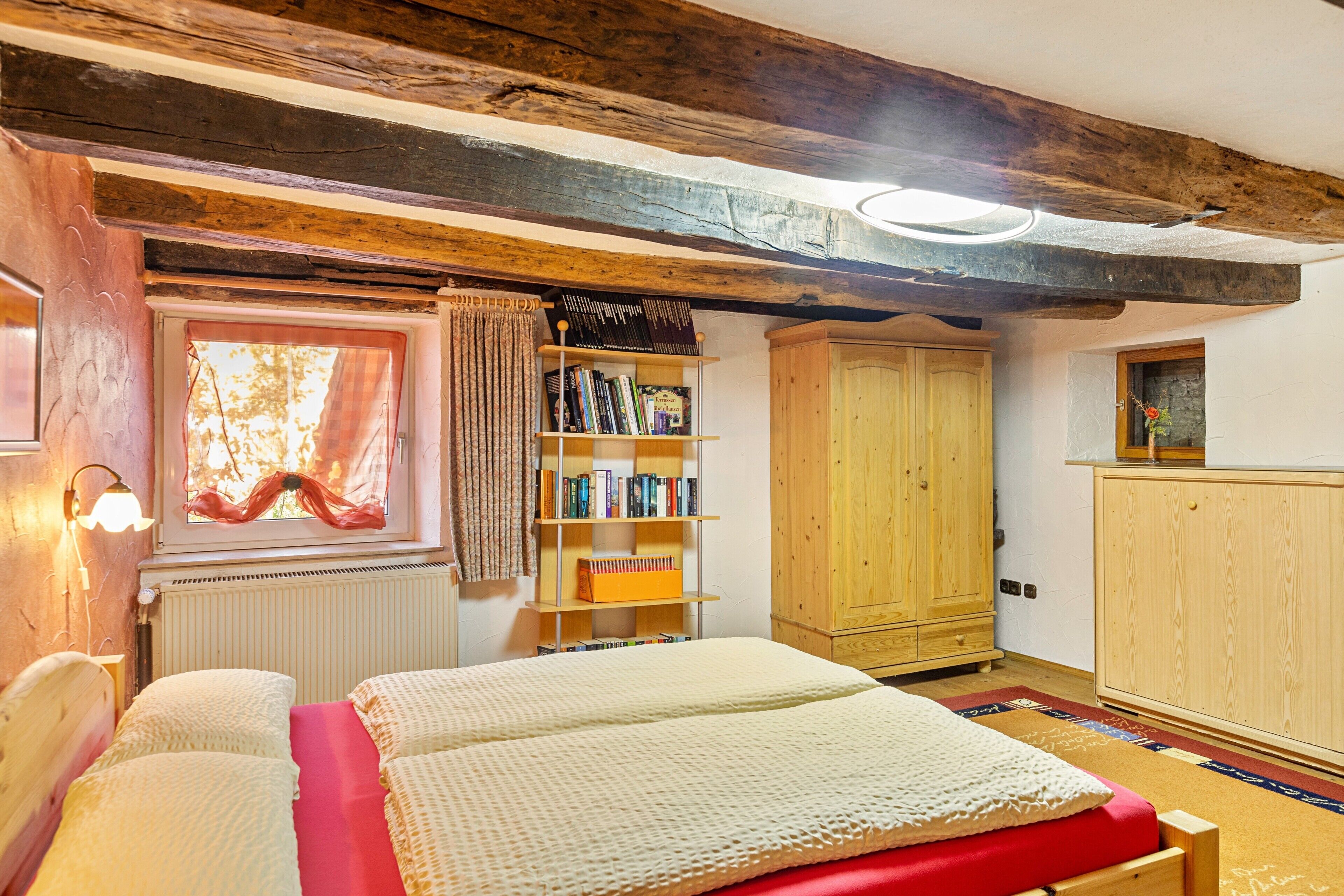 Ein Schlafzimmer mit einem Bett, einem Holzschrank, einem Bücherregal und einem Fenster mit Vorhängen.