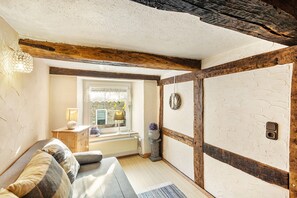 Une pièce avec un plafond en bois, une fenêtre avec des rideaux, un radiateur, un luminaire fixé au mur et une porte ornée d’un motif circulaire.