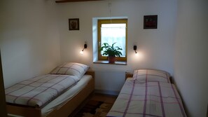 Een kleine kamer met twee enkele bedden, een raam met een plant en wandlampen.