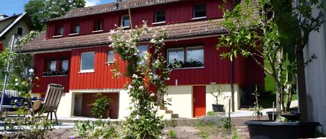 Une maison rouge à deux étages avec un jardin à l’avant.