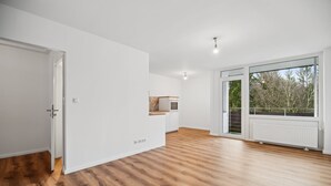 Une pièce spacieuse avec un plancher en bois, un four encastré et une grande porte-fenêtre coulissante donnant sur un balcon avec vue sur les arbres.